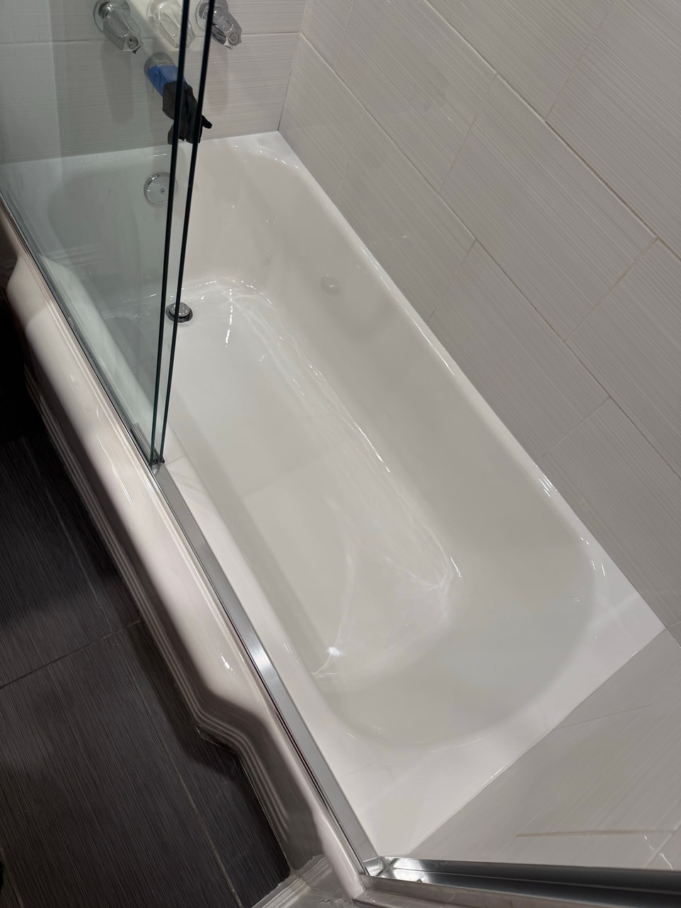 White refinished bathtub with the existing glass door and wall tile