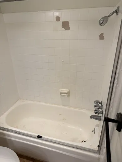Worn bathtub and damaged wall tiles before restoration